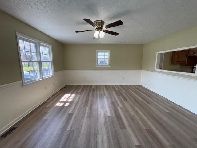 unfurnished room featuring baseboards, a textured ceiling, a ceiling fan, visible vents, and wood finished floors