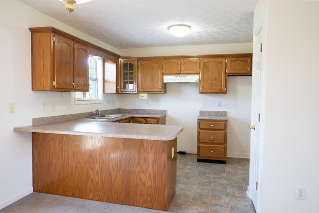 kitchen with a peninsula, brown cabinetry, under cabinet range hood, and a sink