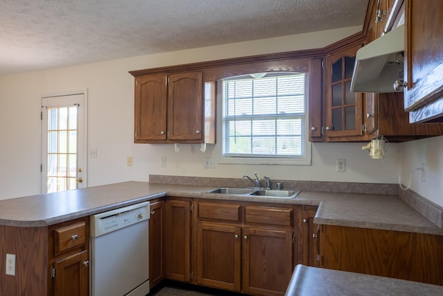 kitchen with under cabinet range hood, a sink, white dishwasher, a peninsula, and brown cabinetry
