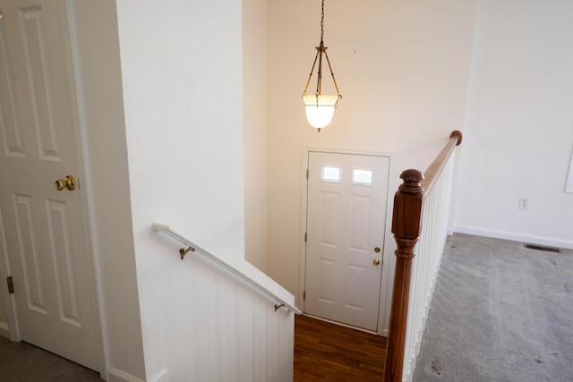 foyer entrance featuring baseboards, visible vents, and dark carpet