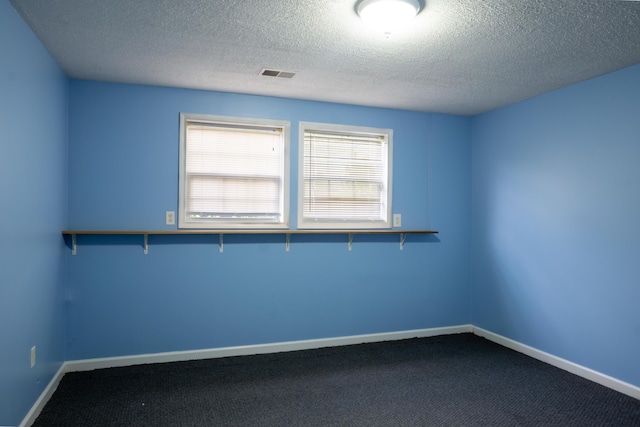 unfurnished room with baseboards, visible vents, dark carpet, and a textured ceiling