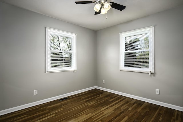 empty room featuring dark wood-type flooring, visible vents, baseboards, and a ceiling fan