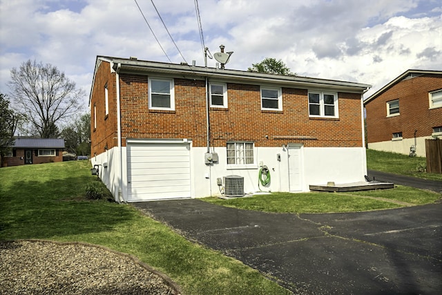 back of house with a garage, a lawn, brick siding, driveway, and central AC unit