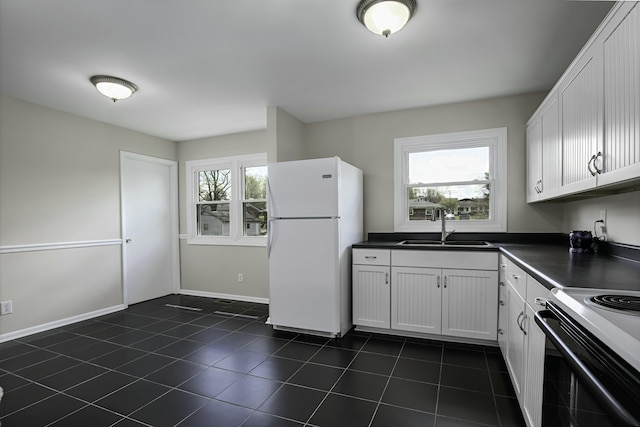kitchen with a sink, white cabinets, freestanding refrigerator, and dark countertops