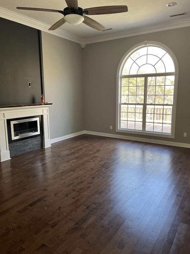 unfurnished living room featuring visible vents, baseboards, dark wood finished floors, crown molding, and a glass covered fireplace