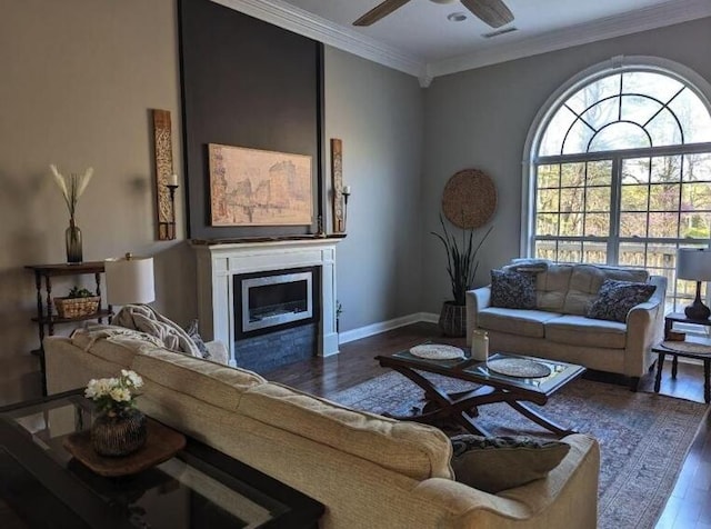living area with visible vents, a ceiling fan, crown molding, wood finished floors, and a glass covered fireplace