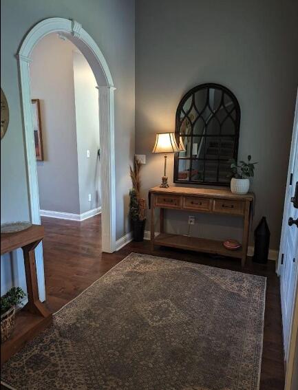 hall featuring arched walkways, wood finished floors, and baseboards