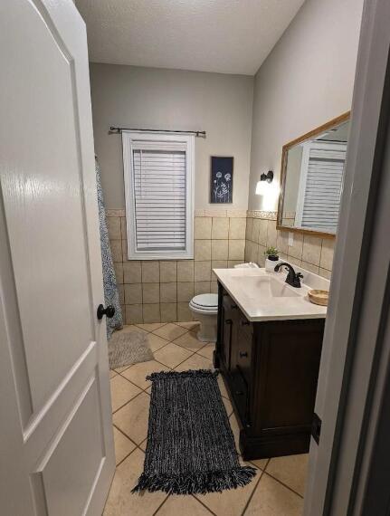 full bath featuring vanity, tile patterned flooring, a wainscoted wall, toilet, and tile walls