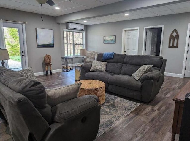 living area with baseboards, a wall mounted air conditioner, a ceiling fan, a paneled ceiling, and wood finished floors
