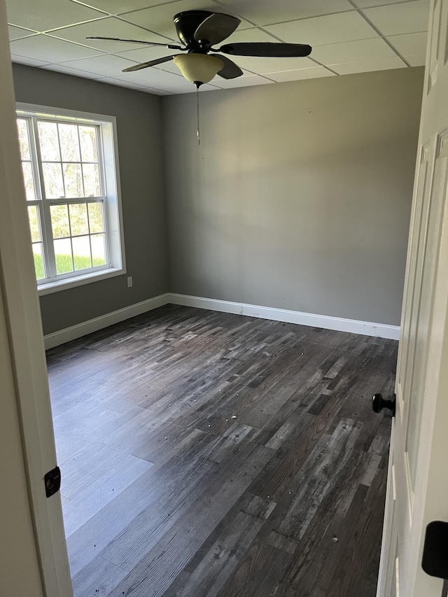 empty room with ceiling fan, a drop ceiling, baseboards, and dark wood finished floors