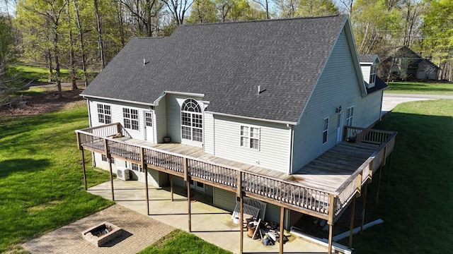 rear view of house featuring a fire pit, a lawn, a patio, a wooden deck, and roof with shingles