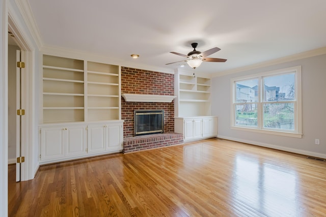 unfurnished living room with light wood-style floors, built in shelves, a ceiling fan, visible vents, and ornamental molding
