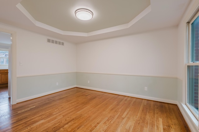 unfurnished room with visible vents, light wood-type flooring, a tray ceiling, and baseboards