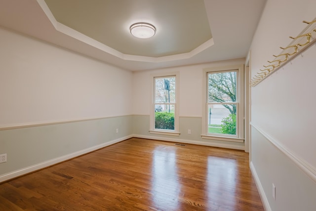 spare room featuring visible vents, baseboards, wood finished floors, and a tray ceiling