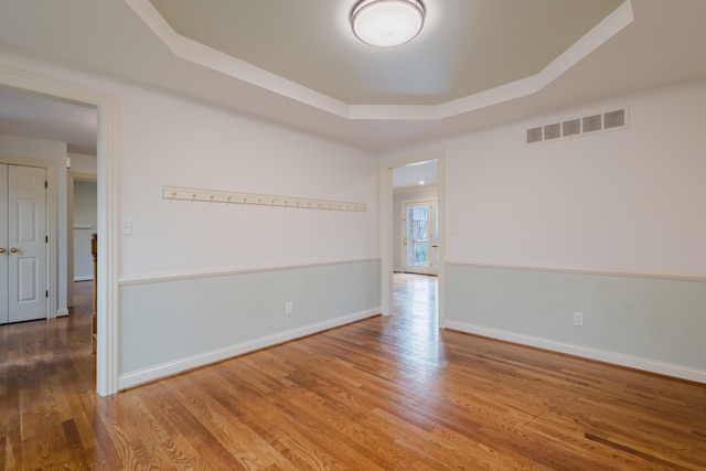 spare room with baseboards, visible vents, wood finished floors, and a tray ceiling