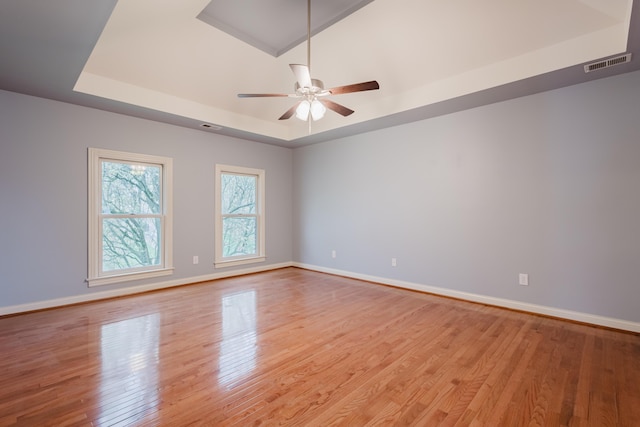 spare room with baseboards, a ceiling fan, light wood-style flooring, and a tray ceiling