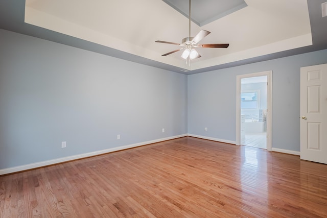empty room featuring ceiling fan, wood finished floors, a raised ceiling, and baseboards