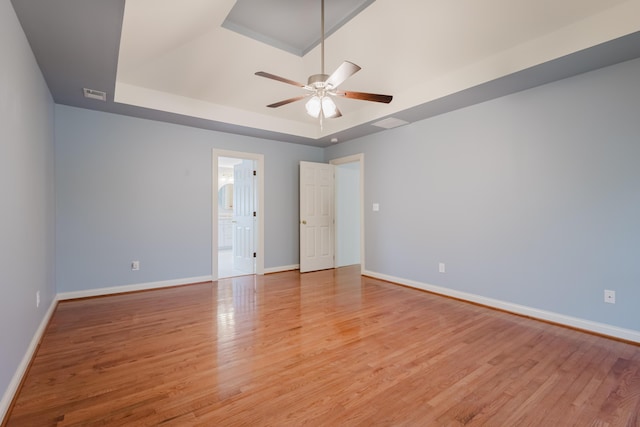 unfurnished bedroom featuring light wood finished floors, ensuite bathroom, baseboards, visible vents, and a raised ceiling