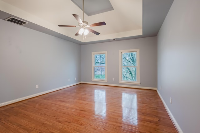 empty room featuring a ceiling fan, visible vents, wood finished floors, and a raised ceiling