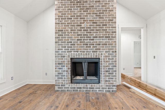 unfurnished living room featuring hardwood / wood-style flooring, lofted ceiling, a brick fireplace, and baseboards
