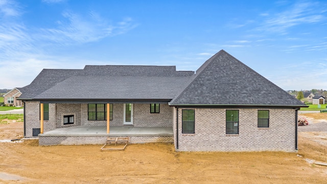 rear view of property featuring brick siding, a shingled roof, and a patio