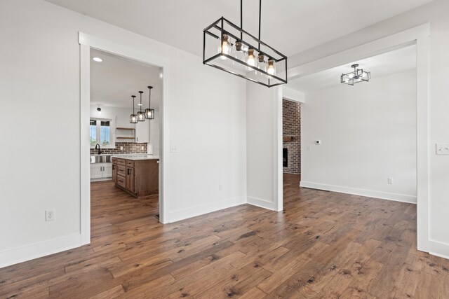 215 Berkley Hall Dr, Berea, KY 40403 - unfurnished dining area featuring a chandelier, dark wood-style flooring, a brick fireplace, baseboards, and a sink