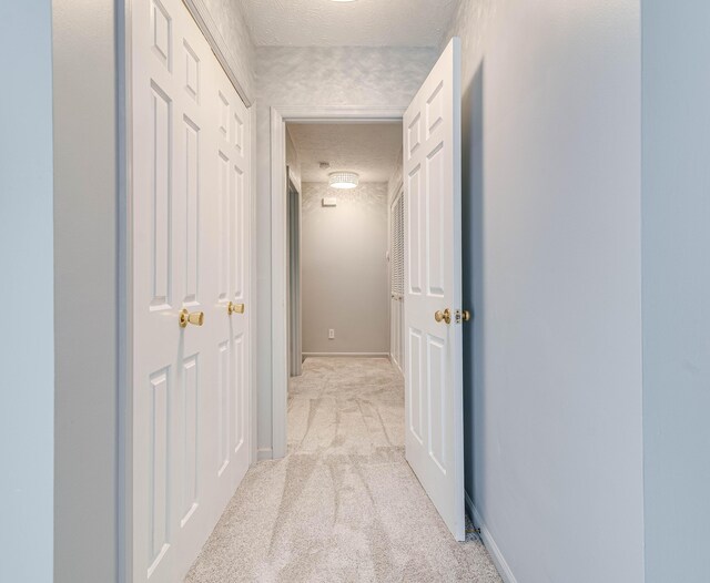 corridor featuring baseboards, light colored carpet, and a textured ceiling