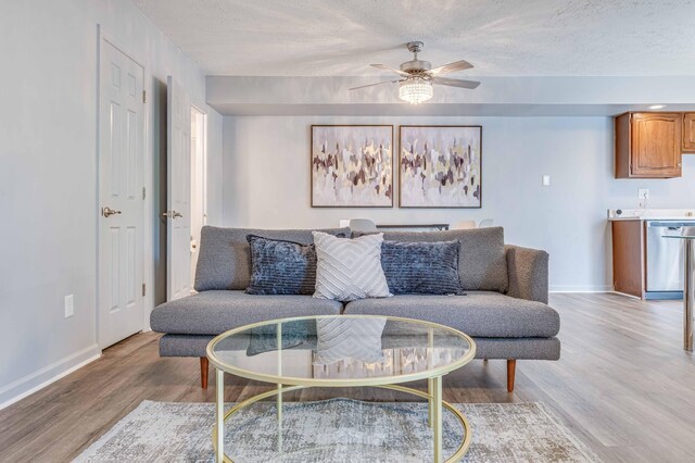 living room featuring light wood-style flooring, a textured ceiling, baseboards, and a ceiling fan