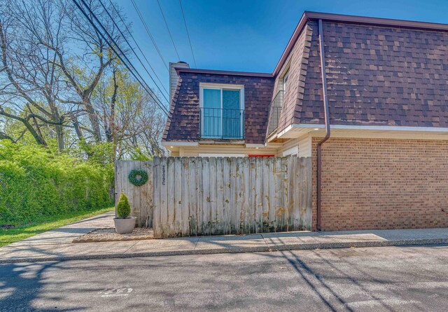 view of side of property with brick siding, a shingled roof, fence, and mansard roof