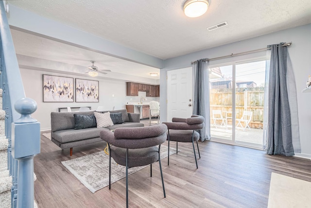 living room with visible vents, baseboards, a ceiling fan, light wood-style floors, and a textured ceiling