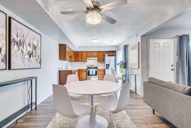 dining area featuring a textured ceiling, ceiling fan, baseboards, and light wood-style floors