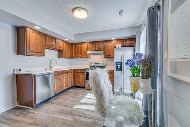 kitchen featuring a sink, light countertops, light wood-type flooring, appliances with stainless steel finishes, and under cabinet range hood