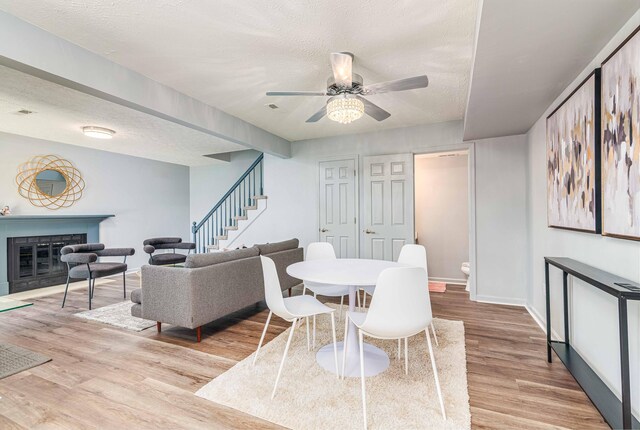 dining area with a textured ceiling, wood finished floors, a ceiling fan, and a glass covered fireplace