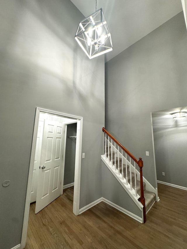 stairway featuring wood finished floors, a high ceiling, baseboards, and an inviting chandelier