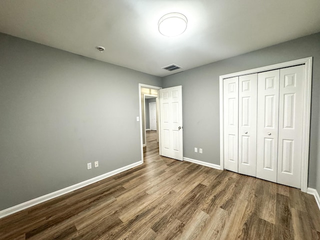 unfurnished bedroom with a closet, wood finished floors, visible vents, and baseboards