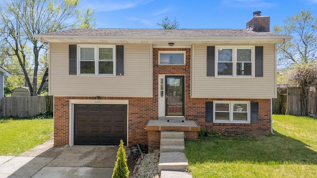 raised ranch with a front lawn, a garage, driveway, brick siding, and fence