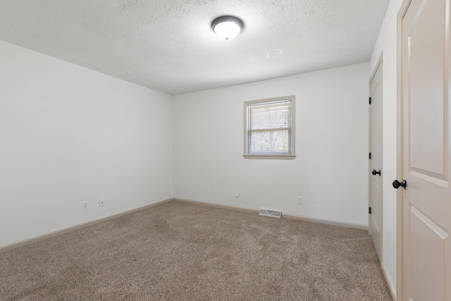 unfurnished room with a textured ceiling, visible vents, baseboards, and carpet floors