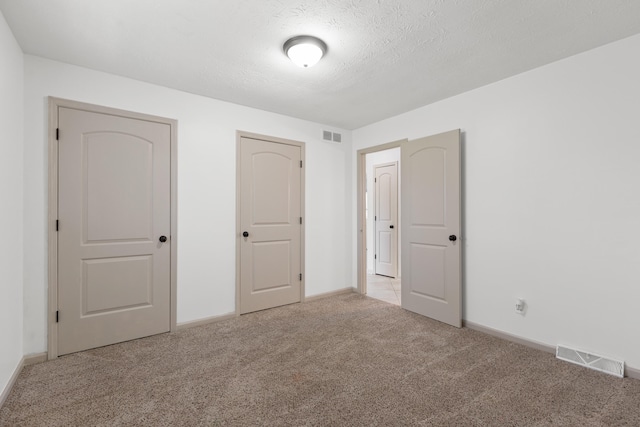 unfurnished bedroom featuring a textured ceiling, visible vents, light carpet, and baseboards