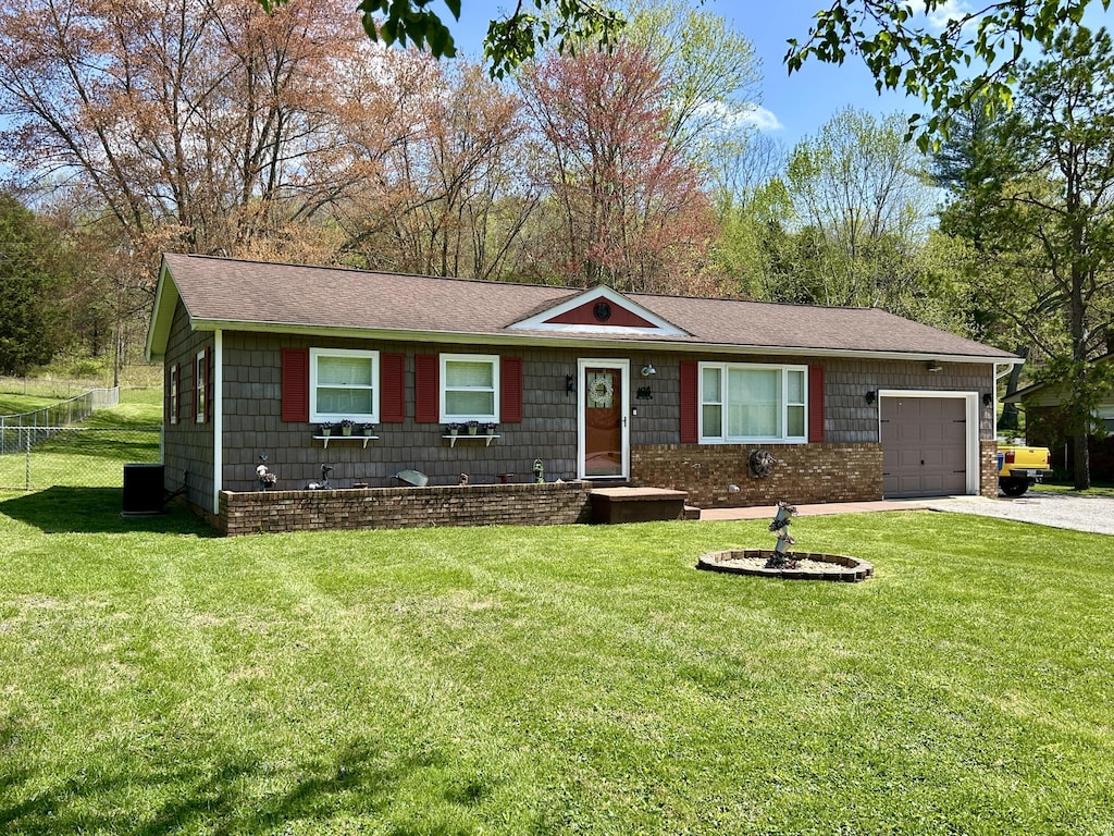 ranch-style house featuring an attached garage, driveway, fence, and a front lawn