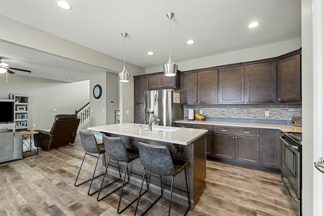 kitchen featuring open floor plan, light wood-style flooring, dark brown cabinets, a breakfast bar area, and appliances with stainless steel finishes