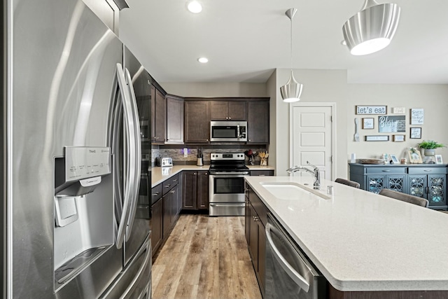 kitchen with a sink, dark brown cabinets, a center island with sink, light wood-style flooring, and stainless steel appliances