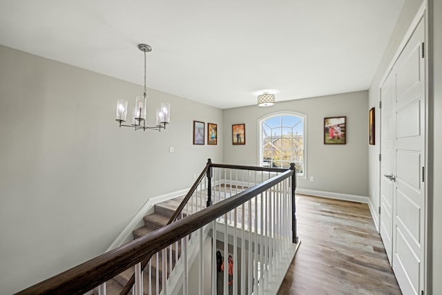 hallway with wood finished floors, baseboards, an upstairs landing, and a notable chandelier