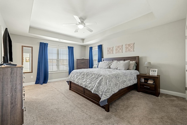 carpeted bedroom with ceiling fan, baseboards, and a raised ceiling
