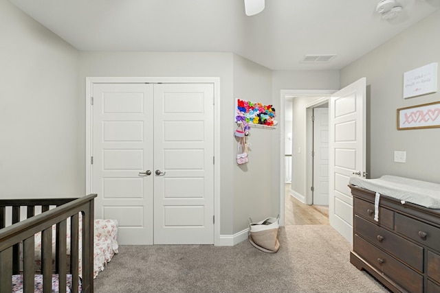 bedroom featuring a closet, visible vents, light carpet, a crib, and baseboards