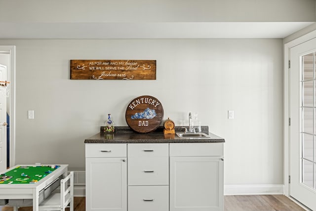 bar featuring indoor wet bar, light wood-style floors, a sink, and baseboards