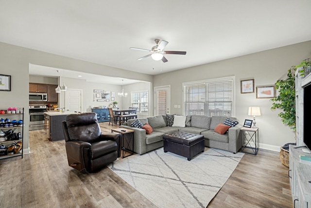 living room with baseboards, light wood finished floors, and ceiling fan with notable chandelier