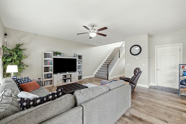 living area featuring stairs, light wood finished floors, baseboards, and ceiling fan