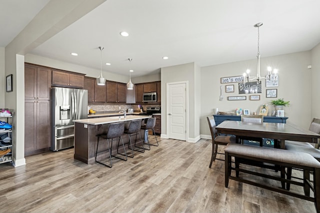 kitchen with a breakfast bar, appliances with stainless steel finishes, light countertops, a center island with sink, and a notable chandelier