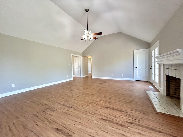 unfurnished living room featuring high vaulted ceiling, a ceiling fan, a tile fireplace, light wood finished floors, and baseboards