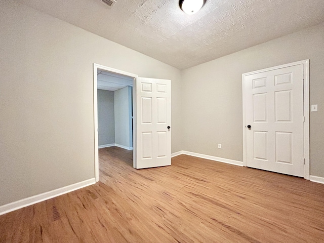 unfurnished room featuring vaulted ceiling, light wood-type flooring, baseboards, and a textured ceiling